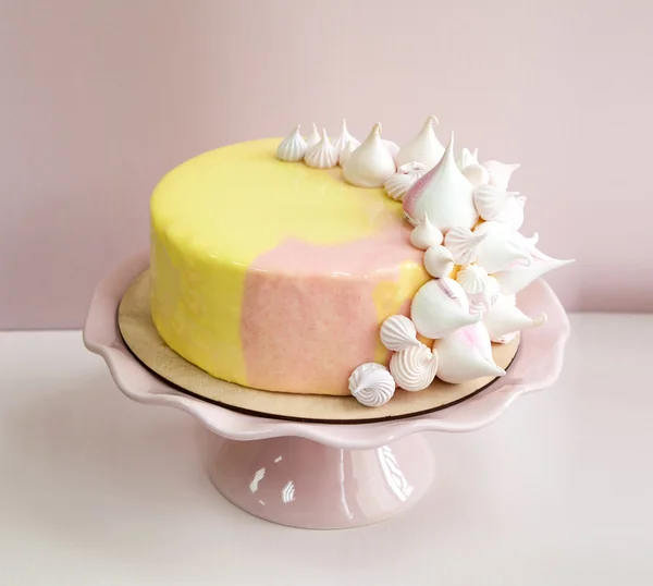 Rosa mousse tårta täckt med gula och rosa choklad mirror glaze och maräng kyssar. Rosa porslin stativ. Rosa bakgrund. Naturligt ljus. — Stockfoto