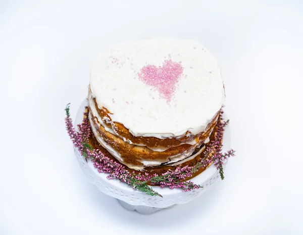 Tarta casera tierna con un corazón rosado en la parte superior y flores de brezo en la parte inferior. Fondo blanco — Foto de Stock