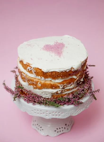 Tarta casera tierna con un corazón rosado en la parte superior y flores de brezo en la parte inferior. Fondo rosa — Foto de Stock