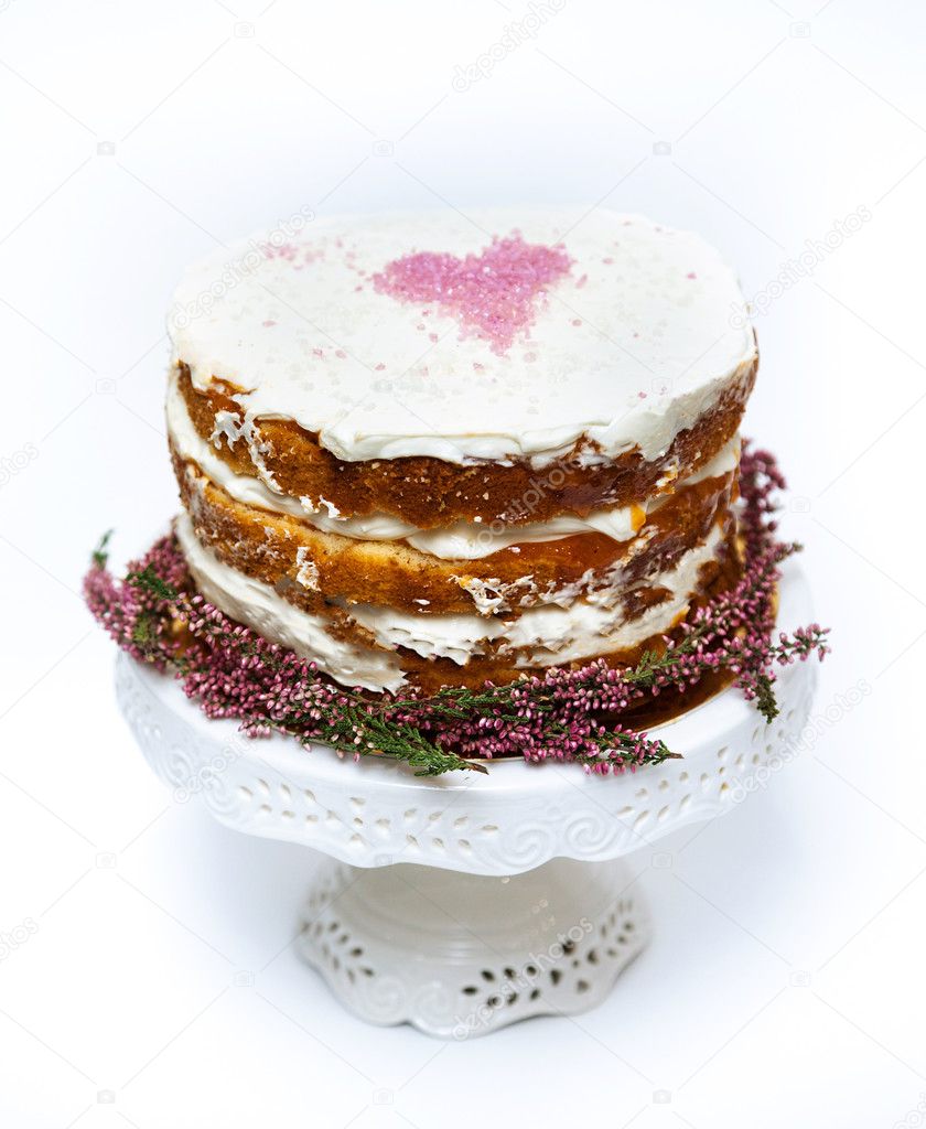 Tender shabby homemade cake with a pink heart on a top and heather flowers on the bottom. White background