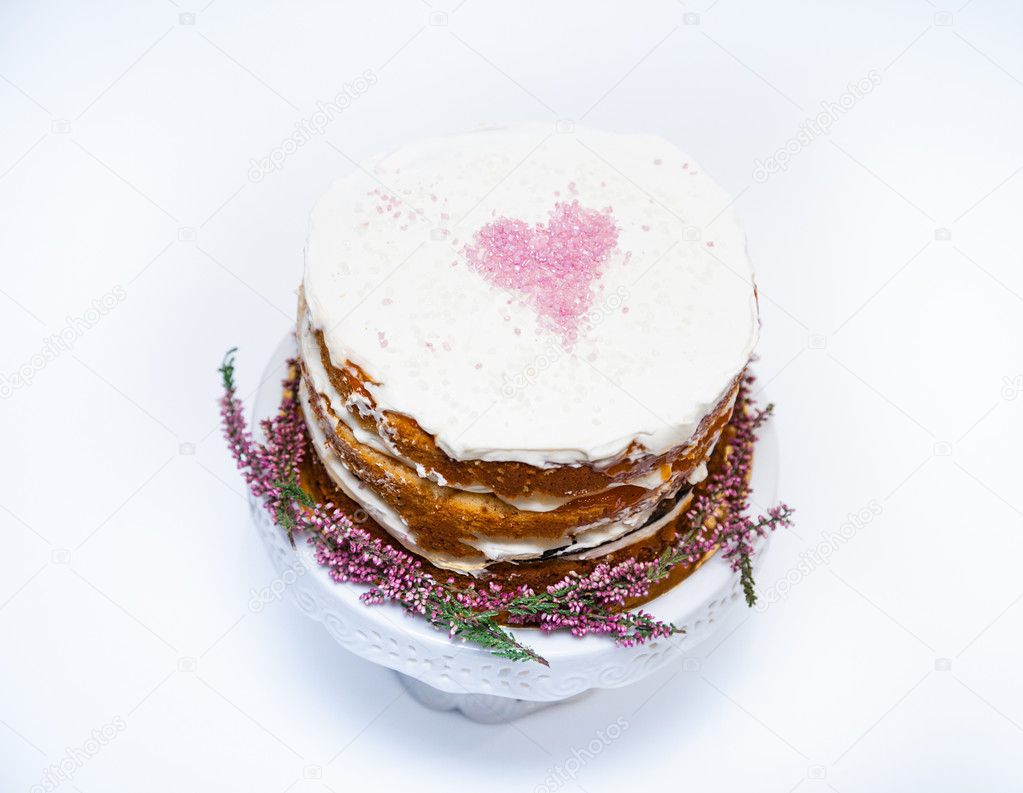 Tender shabby homemade cake with a pink heart on a top and heather flowers on the bottom. White background