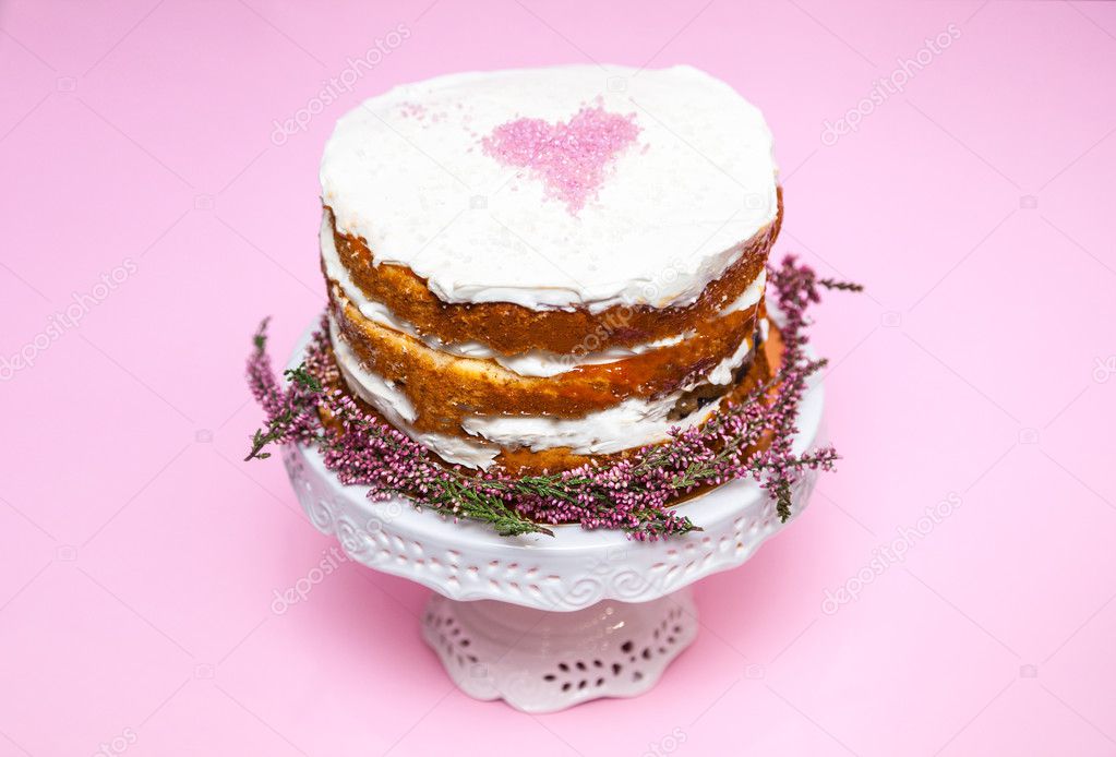Tender shabby homemade cake with a pink heart on a top and heather flowers on the bottom. Pink background