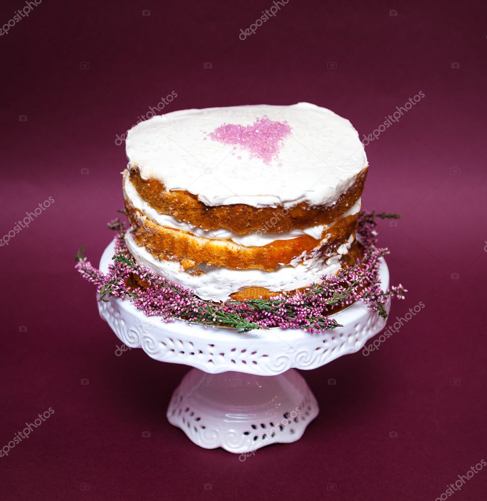 Tender shabby homemade cake with a pink heart on a top and heather flowers on the bottom. Pink background