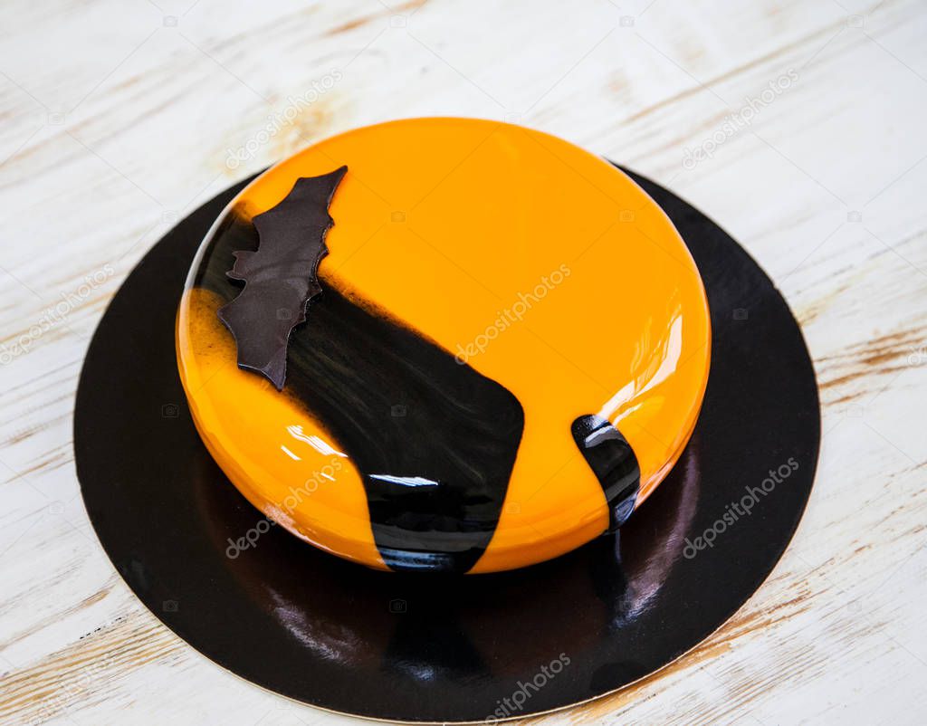 Halloween bright orange and black mousse cake with a chocolate bat decor. Wooden background