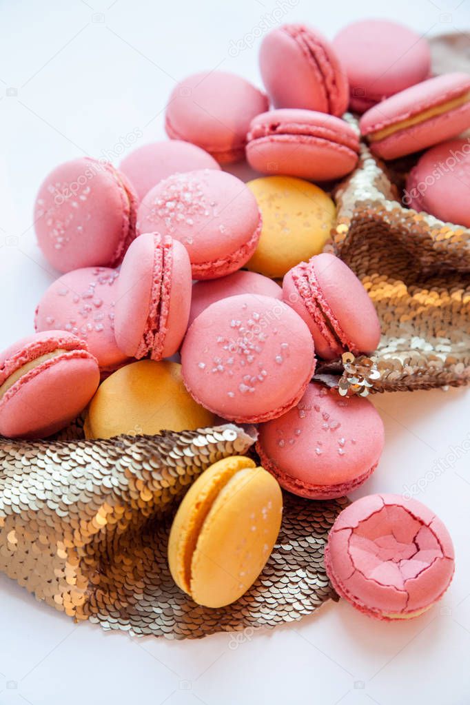 Pink and yellow macaron with golden sequin glitter decor on a white background. Natural light
