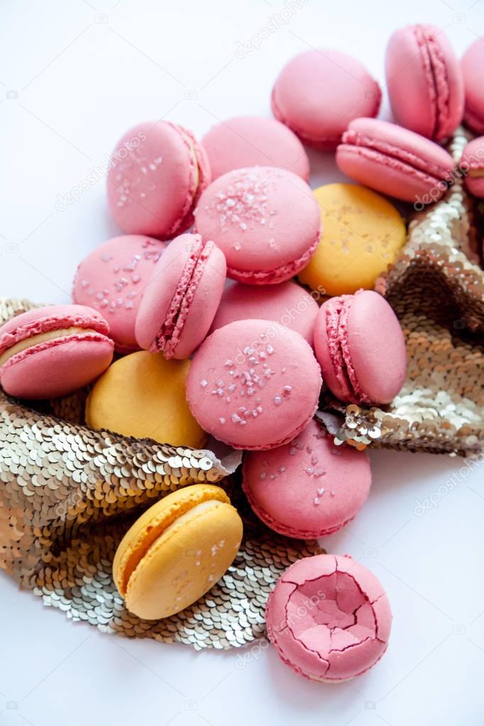 Pink and yellow macaron with golden sequin glitter decor on a white background. Natural light