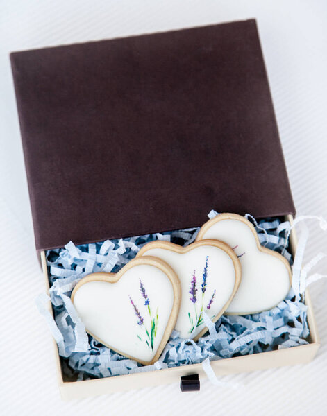 Hand painted cookies topped with white glaze in a gift box. Hand drawn with edible coloring lavender flower stems motive. Natural light
