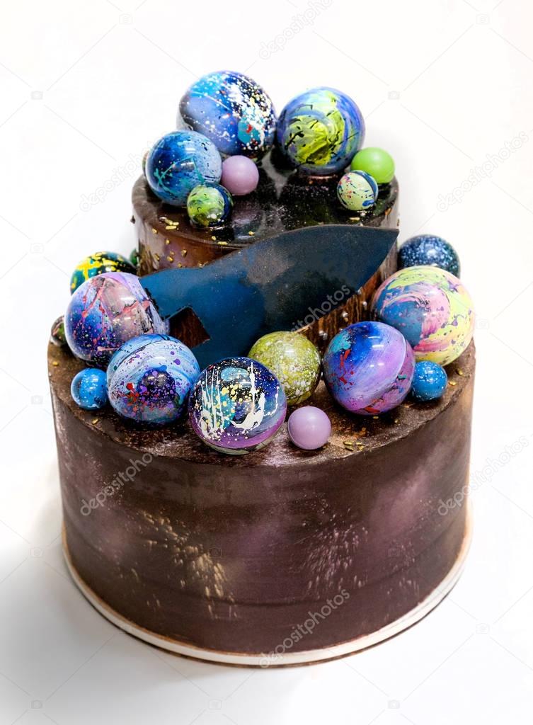 Modern trendy 2-tier layered cake with chocolate hand painted planets and rocket on a white background. 