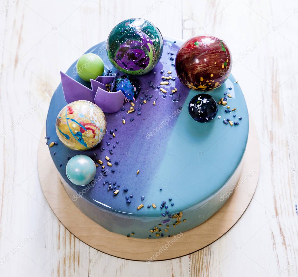 Modern trendy mousse cake with violet blue marble mirror glaze on a white background. Chocolate planet decor. 