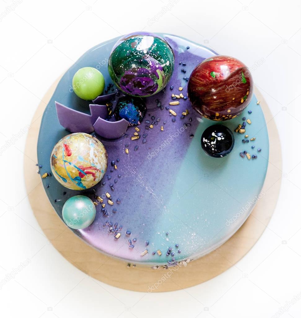 Modern trendy mousse cake with violet blue marble mirror glaze on a white background. Chocolate planet decor. 