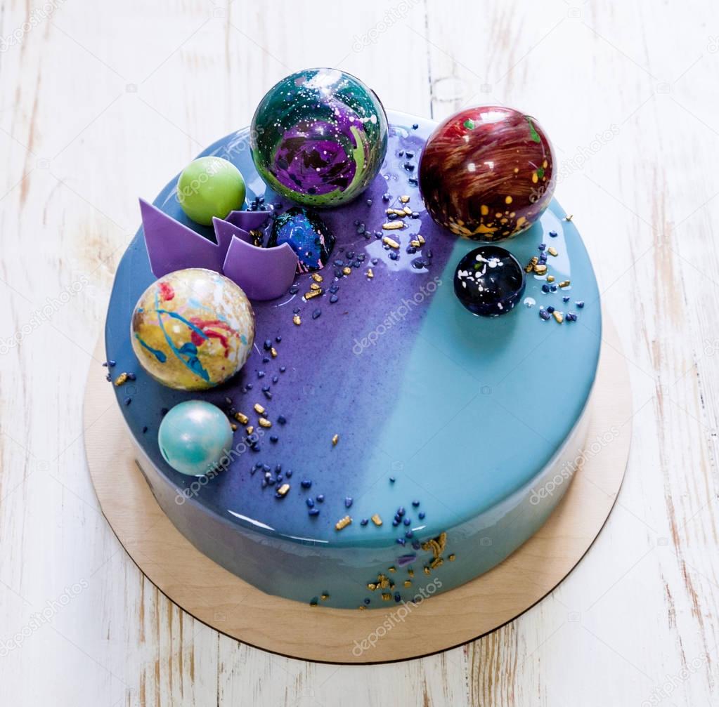 Modern trendy mousse cake with violet blue marble mirror glaze on a white background. Chocolate planet decor. 