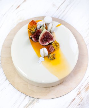 Menekşe beyaz ve turuncu ayna sır üzerinde beyaz bir arka plan ile minimalist mousse kek. Mini macaron, incir ve yenilebilir gümüş dekor. Ahşap arka plan