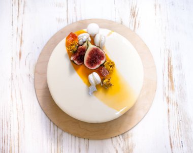 Menekşe beyaz ve turuncu ayna sır üzerinde beyaz bir arka plan ile minimalist mousse kek. Mini macaron, incir ve yenilebilir gümüş dekor. Ahşap arka plan