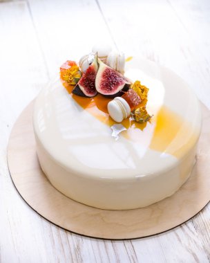 Menekşe beyaz ve turuncu ayna sır üzerinde beyaz bir arka plan ile minimalist mousse kek. Mini macaron, incir ve yenilebilir gümüş dekor. Ahşap arka plan