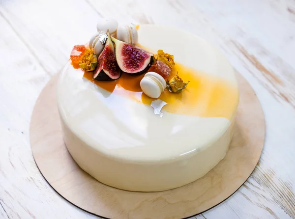 Мінімалістичний торт мусу з фіолетовою білою і помаранчевою дзеркальною глазур'ю на білому тлі. Міні макарон, інжир та їстівний срібний декор. Дерев'яний фон — стокове фото