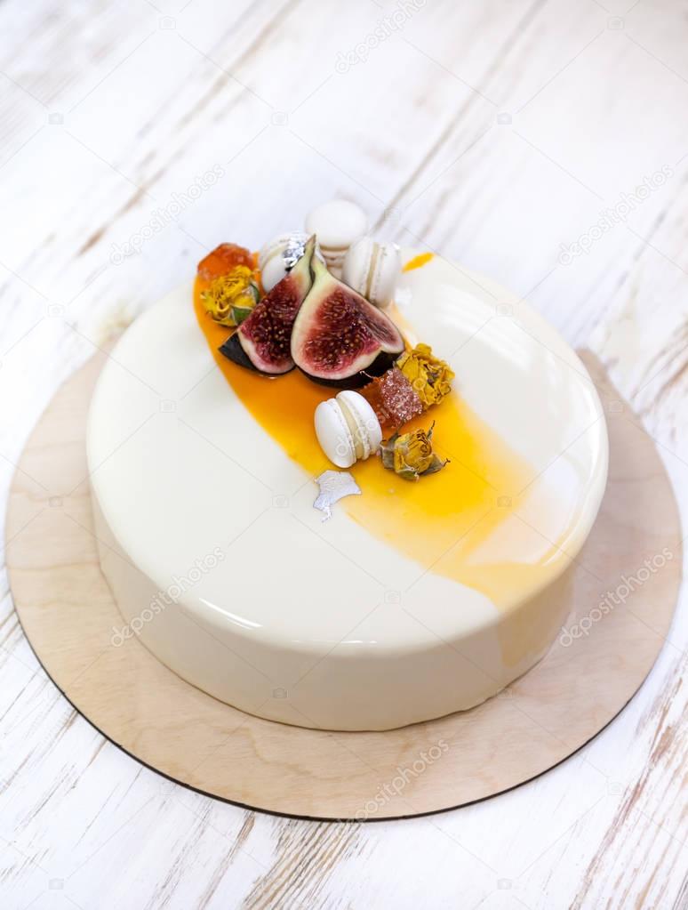 Minimalistic mousse cake with violet white and orange mirror glaze on a white background. Mini macaron, figs and edible silver decor. Wooden background