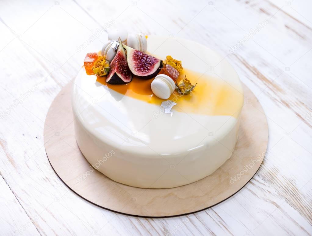 Minimalistic mousse cake with violet white and orange mirror glaze on a white background. Mini macaron, figs and edible silver decor. Wooden background