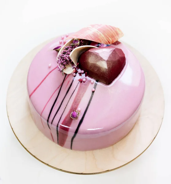 Minimalistic pink mousse cake with coated with mirror glaze on a white background. Chocolate heart, chocolate swirl and dry heather decor. — Stock Photo, Image