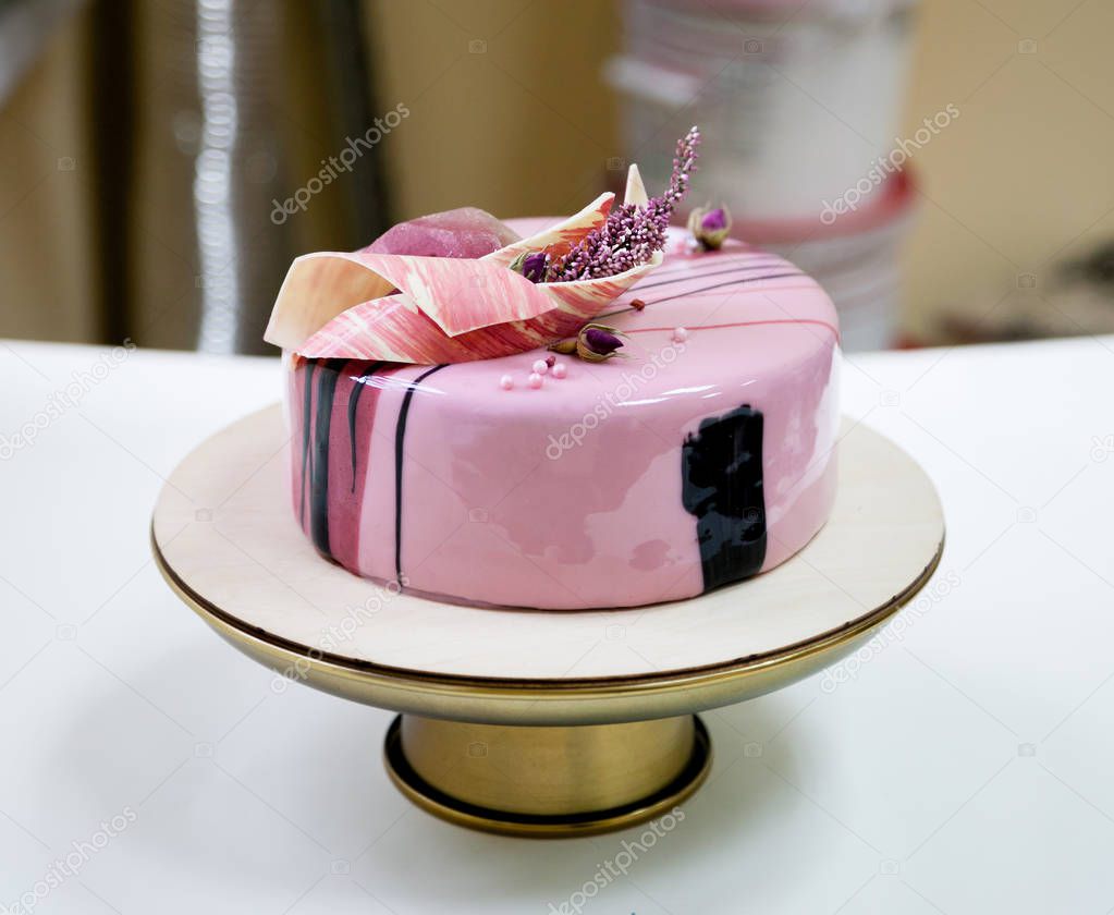 Minimalistic pink mousse cake with coated with mirror glaze on a white background. Chocolate heart, chocolate swirl and dry heather decor.