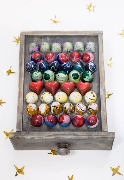 Surtido de bombones de chocolate pintados a mano en una caja de madera. Aislado en blanco con estrellas doradas . — Foto de Stock