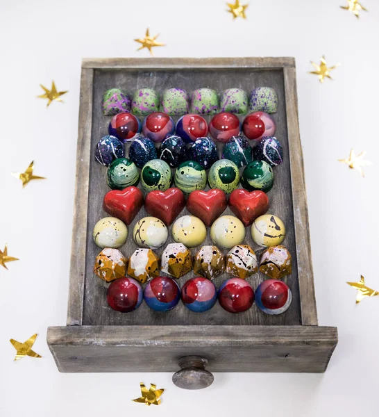 Ποικιλία από σοκολάτα χέρι ζωγραφισμένες καραμέλες καραμέλα σε ένα ξύλινο κουτί. Απομονωμένα σε λευκό με χρυσά αστέρια. — Φωτογραφία Αρχείου