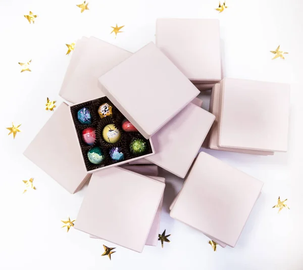 Chocolate hand painted luxury candy bonbons in a pink gift boxes. White background with golden stars.