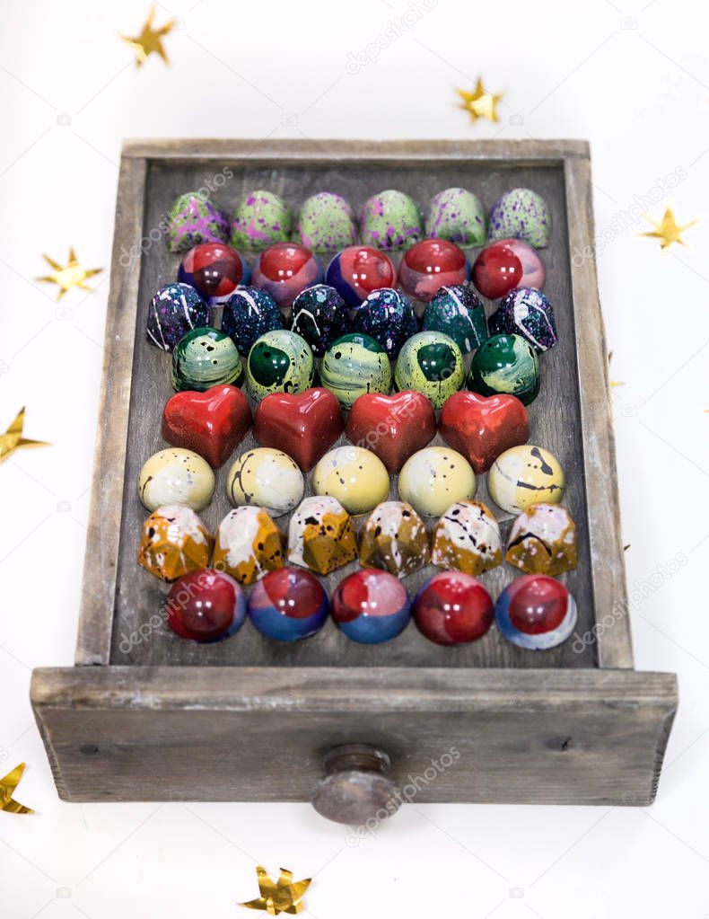 Assortment of chocolate hand painted candy bonbons on a wooden box. Isolated on white with golden stars. 