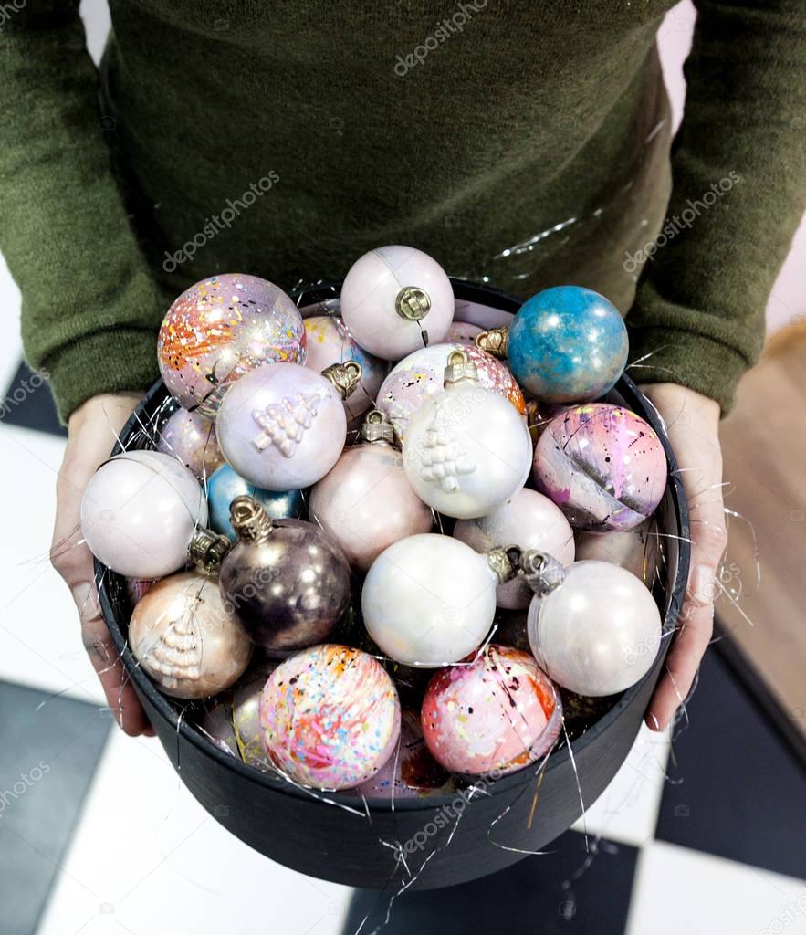 Hands holding christmas hand painted chocolate candy balls in a black gift box. 