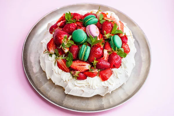 Pavlova meringue cake. Decorated with whipped cream, macaron, strawberries and mint leaves