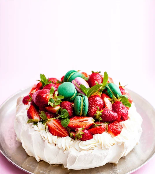 Pavlova meringue cake. Decorated with whipped cream, macaron, strawberries and mint leaves