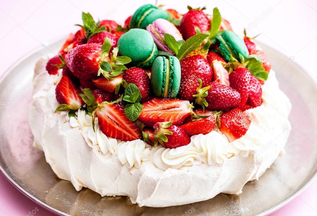 Pavlova meringue cake. Decorated with whipped cream, macaron, strawberries and mint leaves