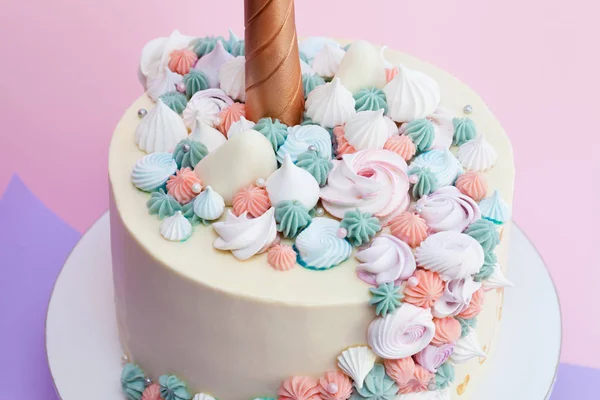 Unicorn layered cake decorated with meringues. Pink background.