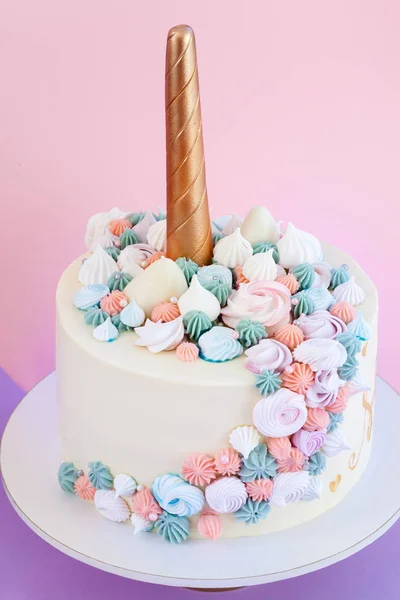 Unicorn layered cake decorated with meringues. Pink background.