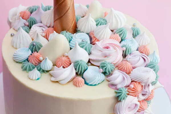 Unicorn layered cake decorated with meringues. Pink background.