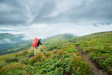 Bulutlar dağların seyahat trekking sopa ve bir sırt çantası ile yürüyor