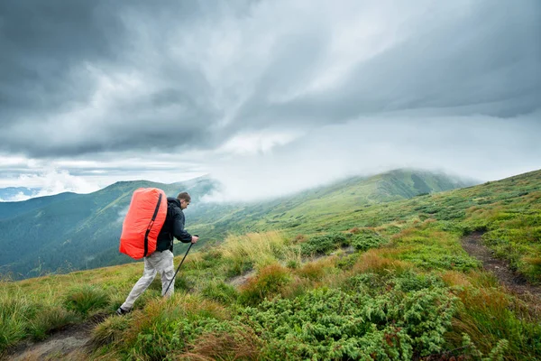 Traveler with trekking sticks and a backpack walks of the mountains in the clouds