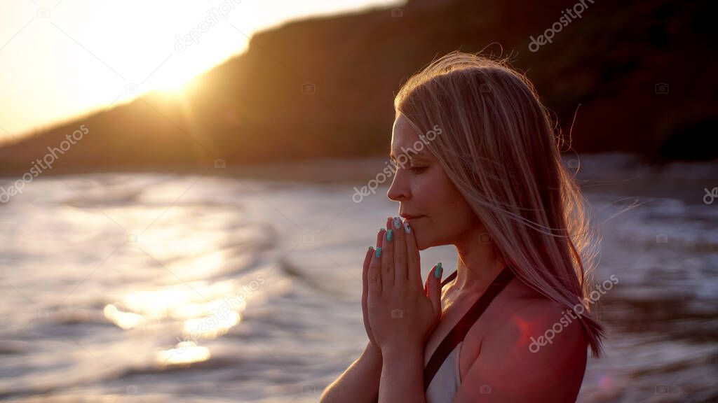 Beautiful woman prays on the sea shore on the sunset