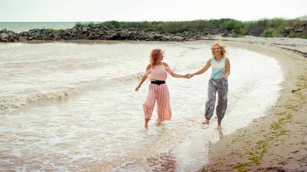 Взрослая дочь и мать, идущие по берегу моря, держась за руки — стоковое фото