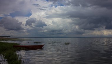 Bulutlu bir günde, tahta kırmızı bir tekne gölde duruyor. Kıyıya demir atmış bir balıkçı teknesi..