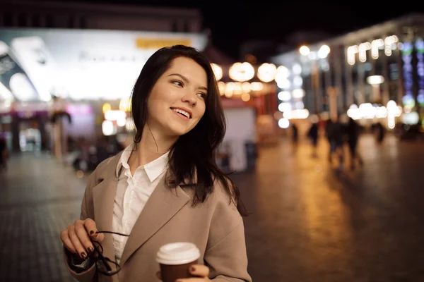 Mujer caminando en la ciudad nocturna y bebiendo café de aroma caliente —  Fotos de Stock