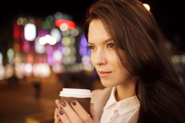 Mujer en la ciudad de noche manteniendo la taza de café y disfrutando de su aroma —  Fotos de Stock