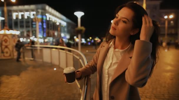 Жінка ходить в нічному місті і розглядає освітлений карусель — стокове відео