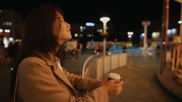 Mujer buscando carrusel iluminado en la ciudad de la noche y beber café aroma — Vídeos de Stock