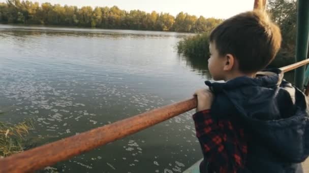 Niño pequeño en un puente mirando el río — Vídeo de stock