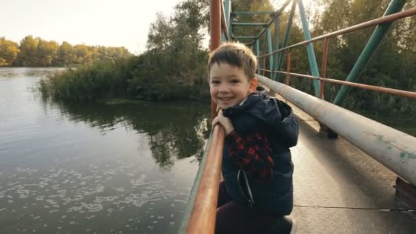 Petit garçon sur un pont regardant la rivière — Video