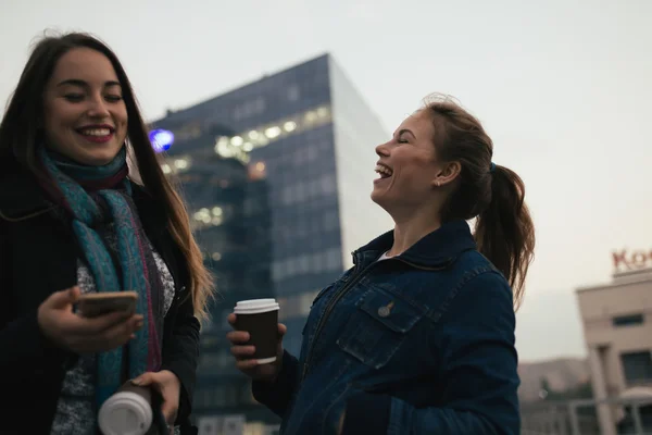 Openlucht portret van twee vrolijke meisjes drinken koffie. Wandelen in een stad. — Stockfoto