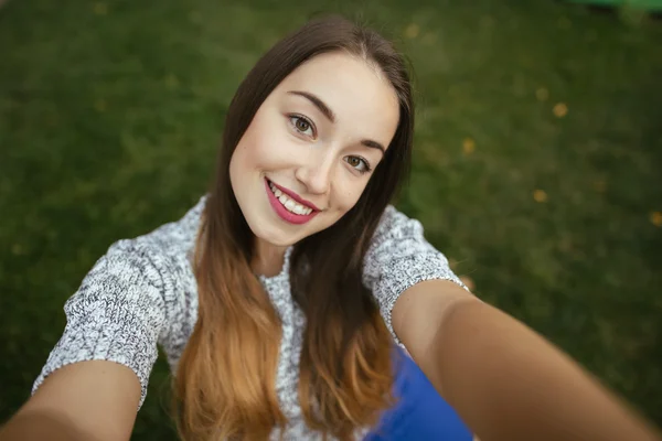 Sevimli gülümseme kadınla çimenlerin üzerinde oturan bir selfie yapmak