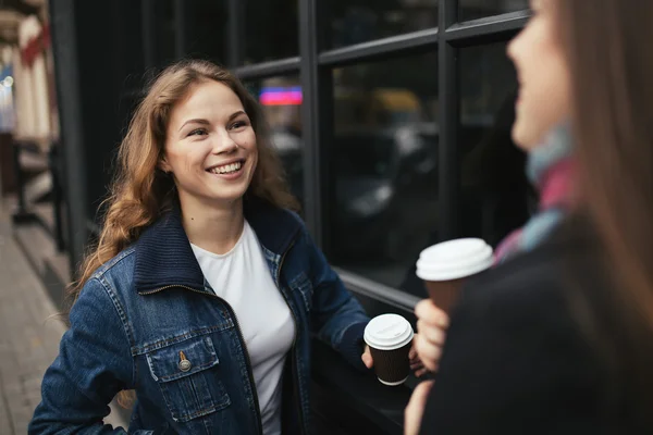 Twee jonge vrouwen zijn blij om te drinken koffie in de stad. Ze houden van een papieren bekers en glimlachen. — Stockfoto