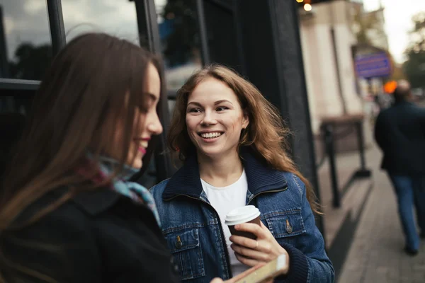 На улице портрет двух женщин, пьющих кофе и смотрящих на смартфон в городе — стоковое фото