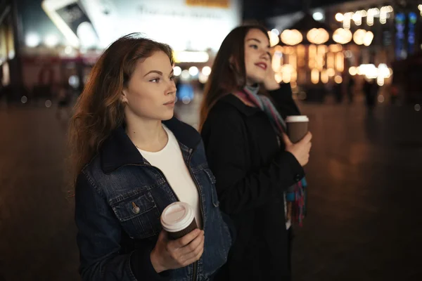 Dos amigas caminando por la calle de la ciudad por la noche y tomando café — Foto de Stock